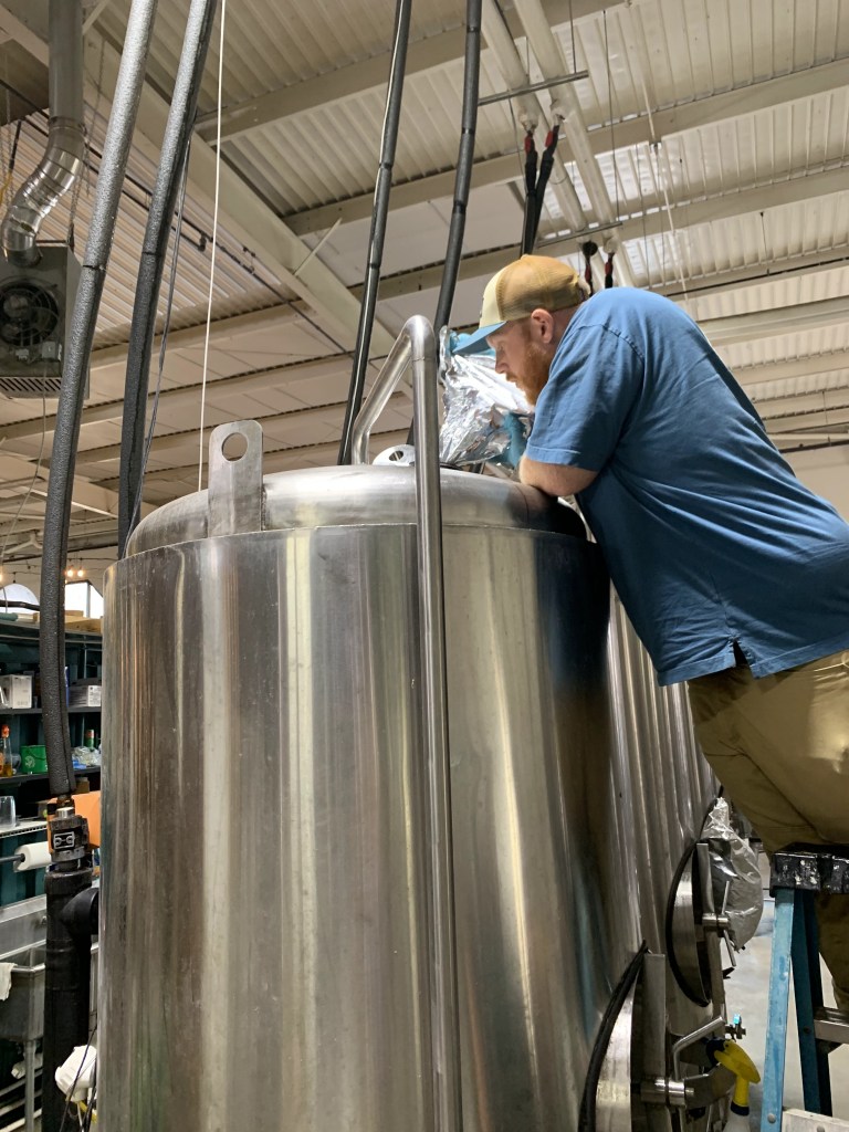 Brewer working over an open stainless fermentation tank